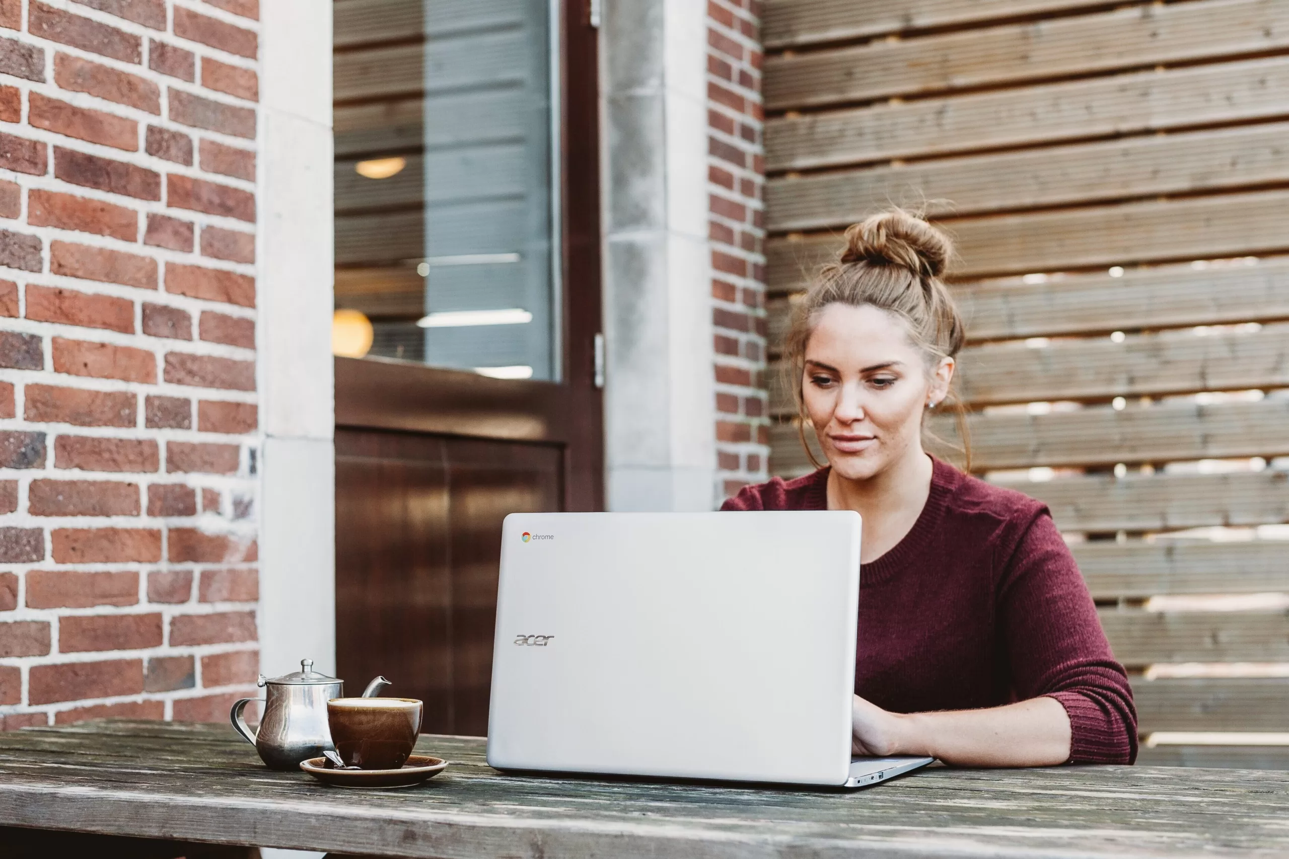 A focused woman typing on a laptop in a cozy coffee shop environment to write blog with images